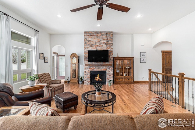 living area with ceiling fan, arched walkways, a brick fireplace, light wood-style floors, and recessed lighting