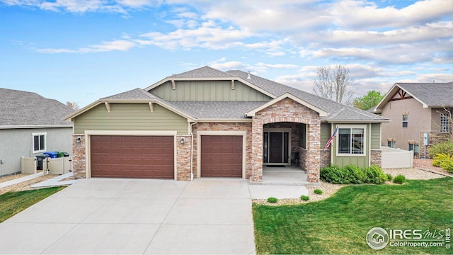 craftsman inspired home featuring roof with shingles, a front lawn, concrete driveway, an attached garage, and stone siding