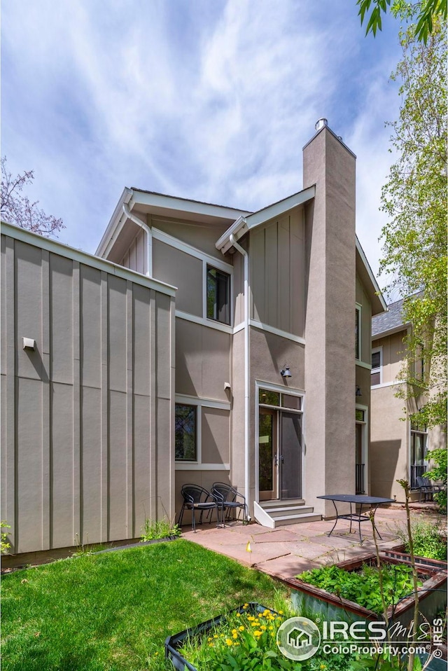 back of property with board and batten siding, a chimney, a patio area, and stucco siding