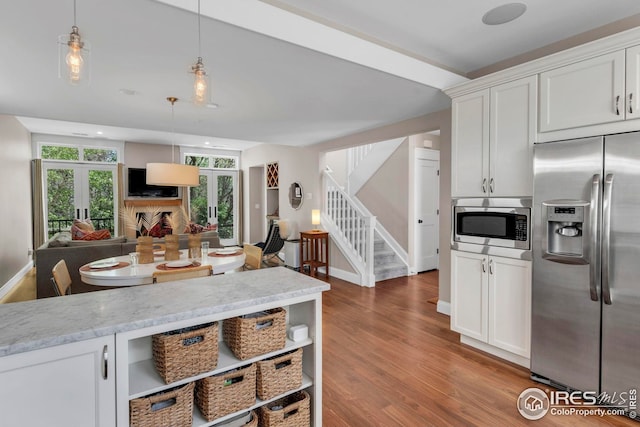 kitchen with hanging light fixtures, light stone countertops, wood finished floors, stainless steel appliances, and white cabinetry