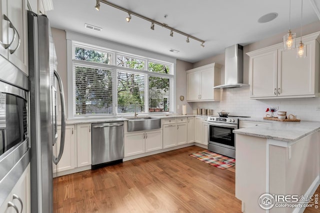 kitchen featuring appliances with stainless steel finishes, wall chimney exhaust hood, white cabinetry, a sink, and light wood-style flooring
