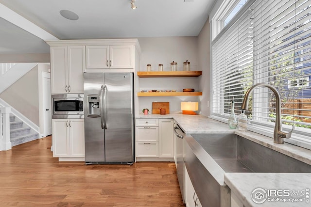 kitchen featuring white cabinets, stainless steel appliances, light stone countertops, and a sink
