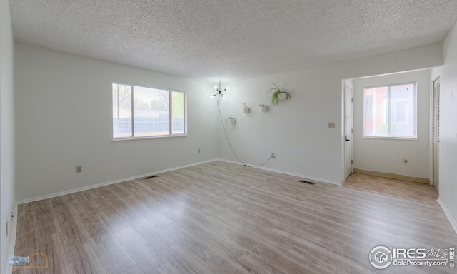 unfurnished room with a textured ceiling, light wood finished floors, and a wealth of natural light