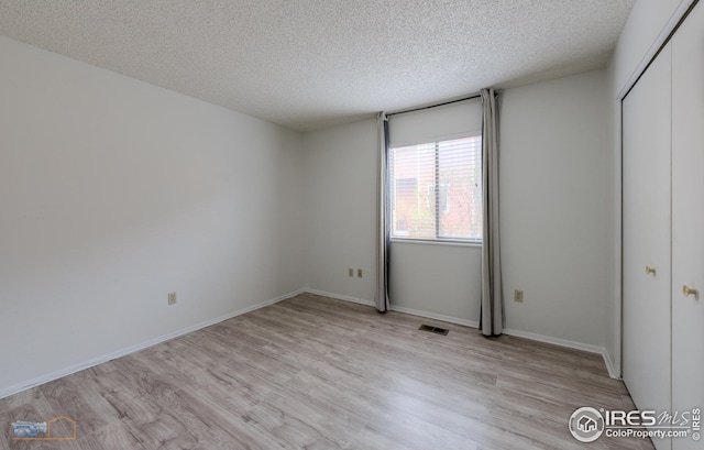 unfurnished bedroom with light wood-style floors, a closet, a textured ceiling, and visible vents
