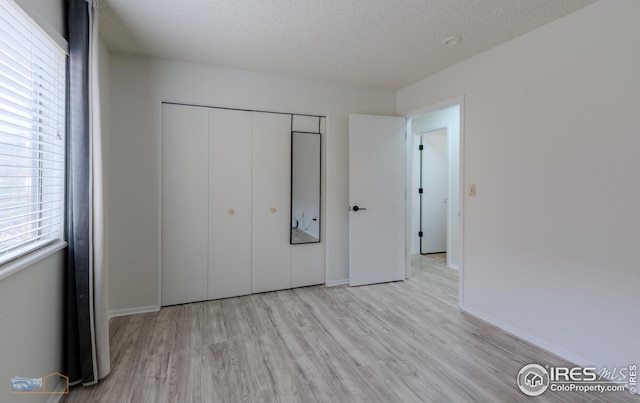 unfurnished bedroom featuring a textured ceiling, baseboards, a closet, and wood finished floors