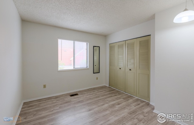 unfurnished bedroom with visible vents, a closet, light wood-style floors, baseboards, and a textured ceiling