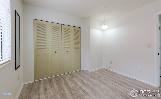 unfurnished bedroom with a closet, a textured ceiling, light wood finished floors, and baseboards