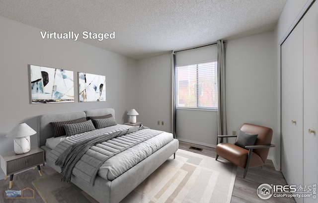 bedroom featuring a textured ceiling, baseboards, wood finished floors, visible vents, and a closet
