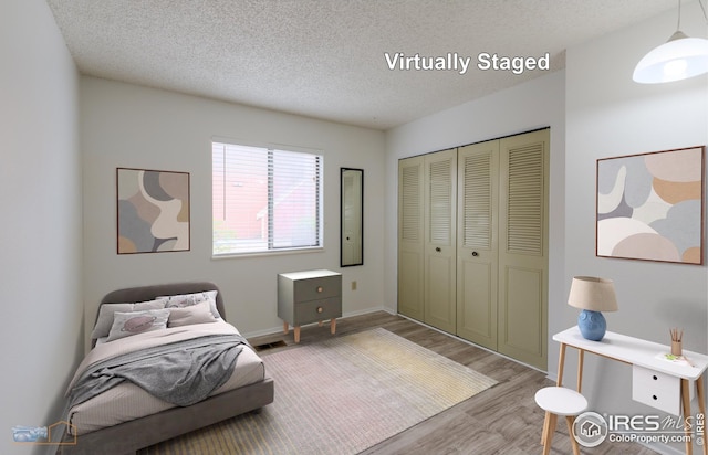 bedroom with a textured ceiling, visible vents, wood finished floors, baseboards, and a closet