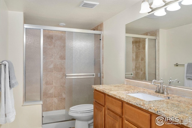 bathroom with vanity, a shower stall, toilet, and visible vents