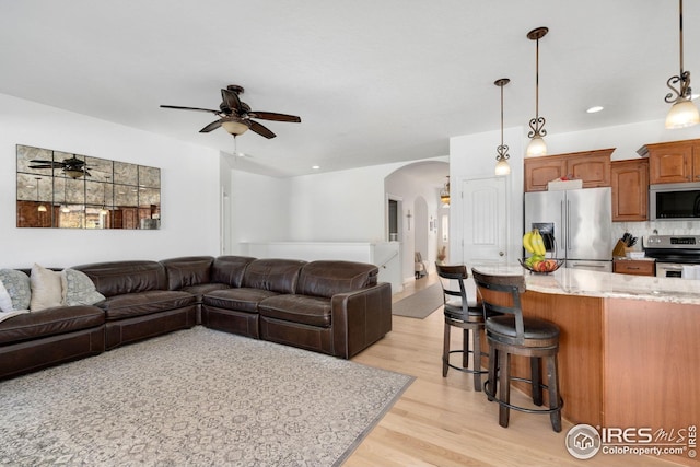 living area featuring arched walkways, a ceiling fan, recessed lighting, and light wood-style flooring