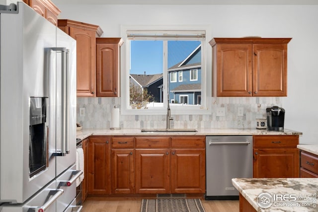kitchen with a sink, light stone counters, light wood-style floors, and stainless steel appliances