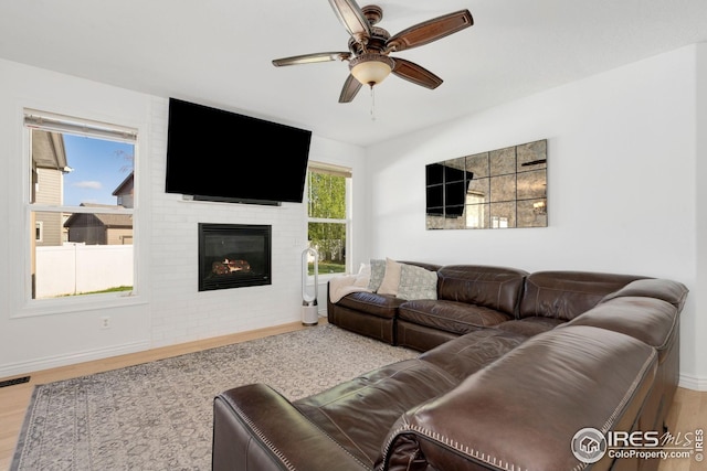 living area featuring baseboards, a ceiling fan, wood finished floors, and a brick fireplace