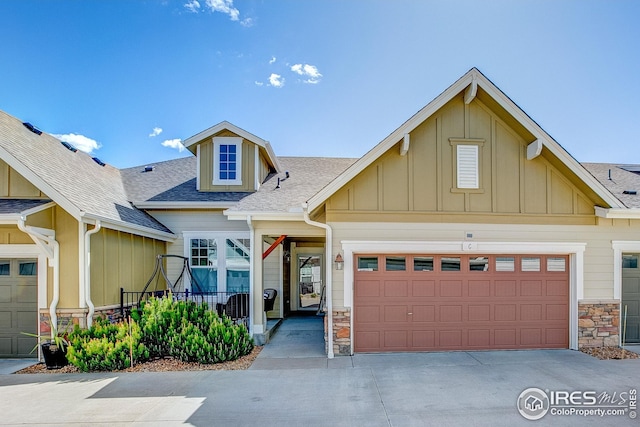craftsman-style house featuring a shingled roof, board and batten siding, concrete driveway, and stone siding