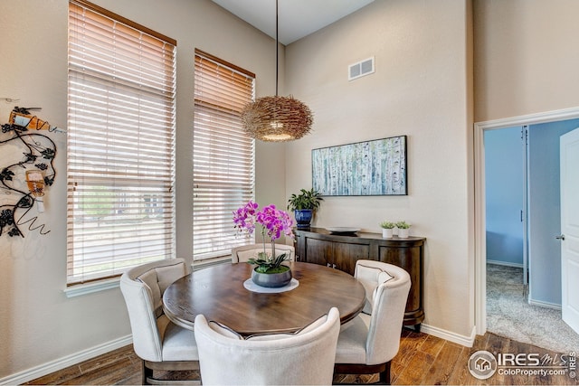 dining space featuring baseboards, visible vents, wood finished floors, and a towering ceiling