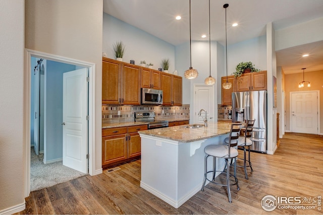 kitchen featuring brown cabinets, a sink, light wood-style floors, a high ceiling, and stainless steel appliances