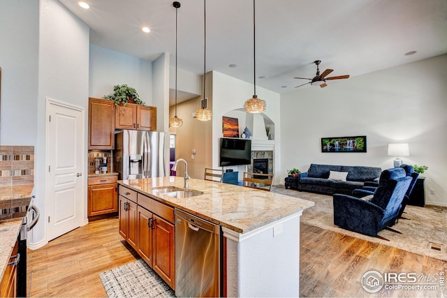 kitchen with a sink, light stone countertops, a ceiling fan, light wood-style flooring, and appliances with stainless steel finishes