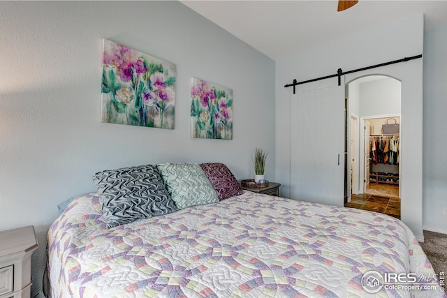 carpeted bedroom with a barn door, a ceiling fan, and a walk in closet