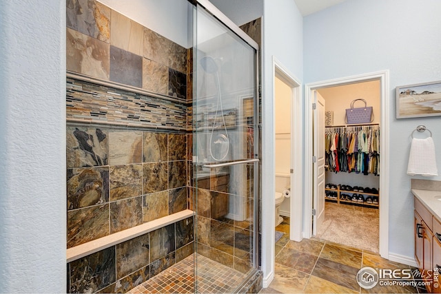 full bathroom with vanity, a shower stall, toilet, and a spacious closet