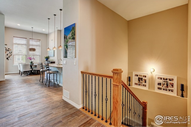 hallway featuring wood finished floors, a sink, baseboards, an upstairs landing, and recessed lighting