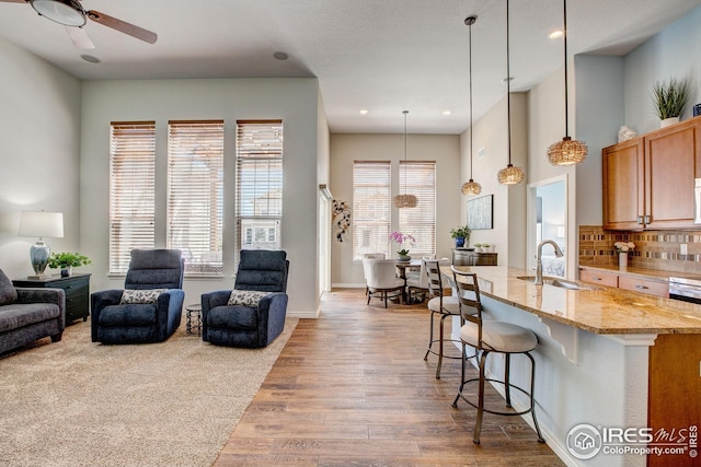 kitchen featuring a kitchen bar, a sink, light stone counters, open floor plan, and light wood-style floors
