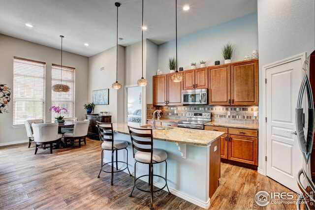 kitchen featuring a high ceiling, light stone counters, a sink, brown cabinetry, and stainless steel appliances