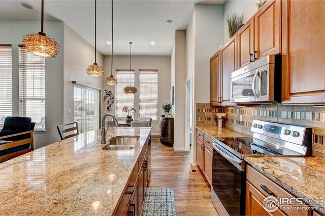 kitchen featuring light stone countertops, light wood-type flooring, tasteful backsplash, a sink, and stainless steel appliances