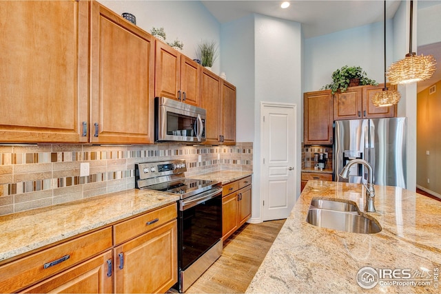 kitchen featuring hanging light fixtures, light wood-type flooring, a sink, light stone counters, and stainless steel appliances