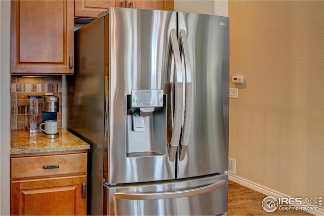 kitchen featuring wood finished floors, baseboards, stainless steel fridge, tasteful backsplash, and light stone counters
