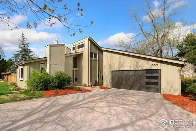 mid-century inspired home featuring a garage, a chimney, and driveway