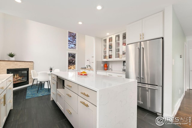 kitchen with decorative backsplash, high end refrigerator, glass insert cabinets, recessed lighting, and white cabinetry