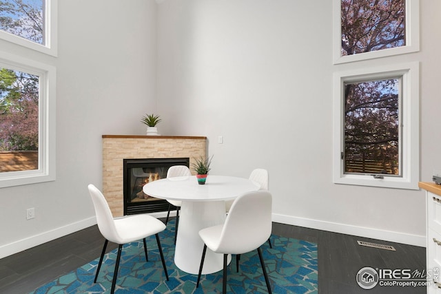 dining room with dark wood-type flooring, baseboards, a glass covered fireplace, and a high ceiling