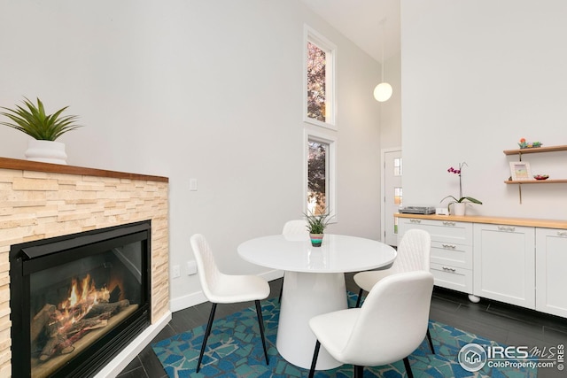 dining area with a fireplace, dark wood-style flooring, and a towering ceiling