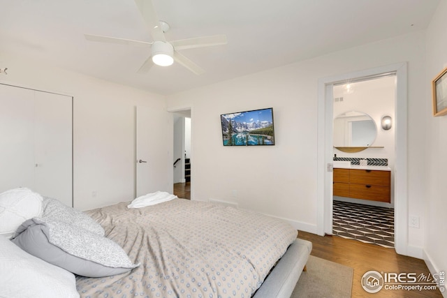 bedroom with a closet, wood finished floors, ensuite bathroom, baseboards, and ceiling fan