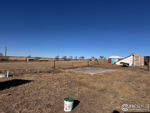 view of yard featuring fence, an outbuilding, and a rural view