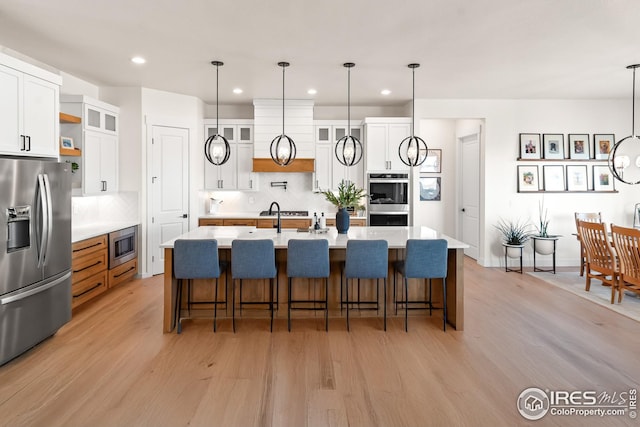 kitchen with light countertops, appliances with stainless steel finishes, decorative backsplash, and light wood-type flooring