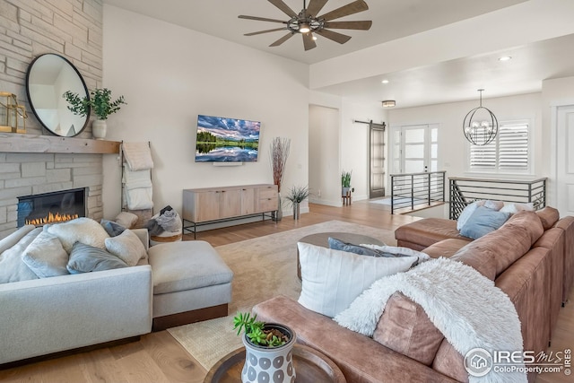 living area featuring a barn door, a stone fireplace, ceiling fan with notable chandelier, recessed lighting, and wood finished floors