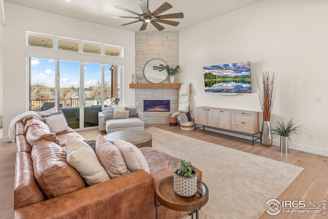 living area featuring baseboards, ceiling fan, a stone fireplace, and wood finished floors