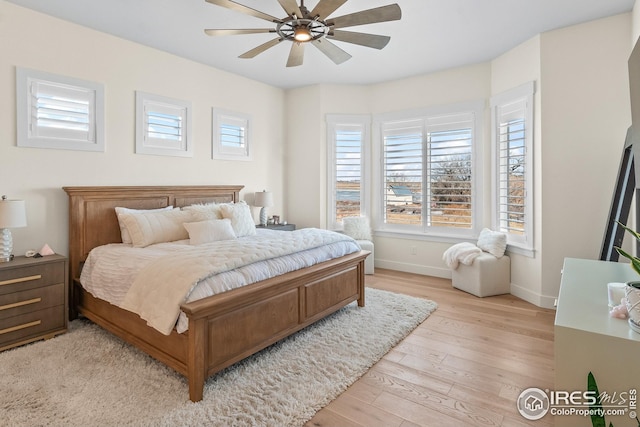 bedroom featuring baseboards, ceiling fan, multiple windows, and light wood-style flooring