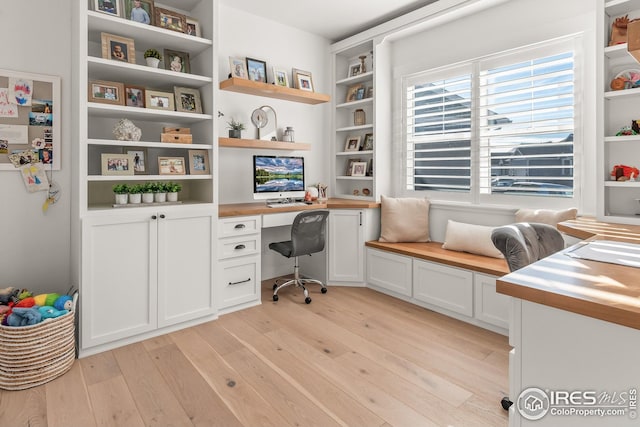 home office featuring light wood finished floors, built in desk, and built in features