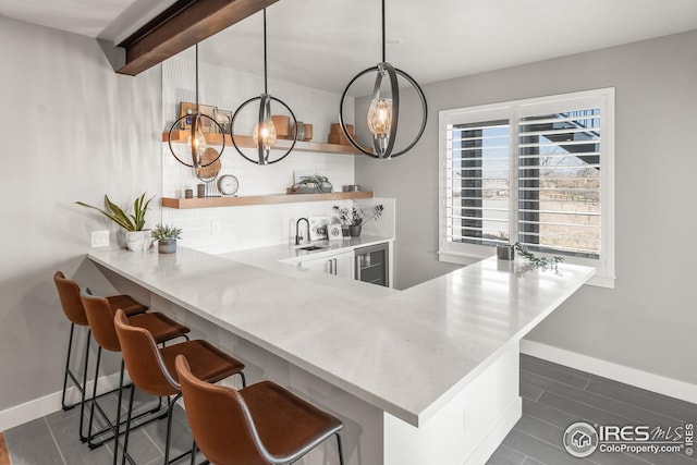 bar featuring a notable chandelier, a sink, beverage cooler, baseboards, and tasteful backsplash