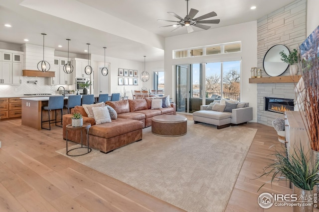 living area with recessed lighting, ceiling fan, a stone fireplace, and light wood-style floors