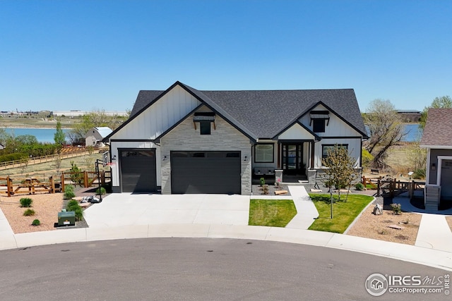 view of front facade with a shingled roof, an attached garage, stone siding, a water view, and driveway