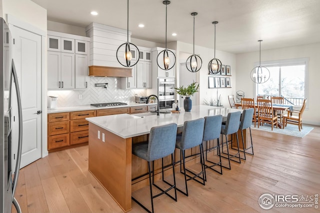 kitchen featuring a sink, light wood-style floors, an island with sink, stainless steel appliances, and tasteful backsplash