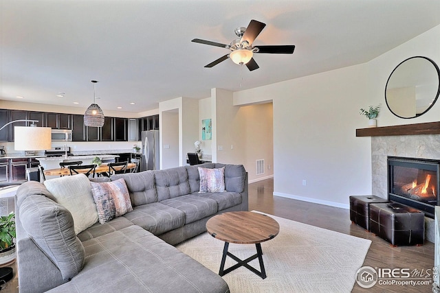 living room featuring visible vents, wood finished floors, baseboards, ceiling fan, and a tiled fireplace