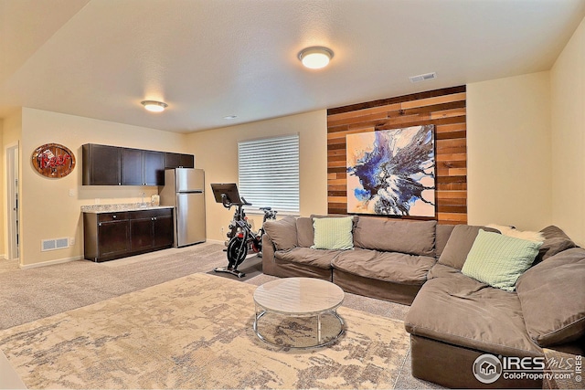 living area with visible vents, baseboards, wooden walls, and light colored carpet