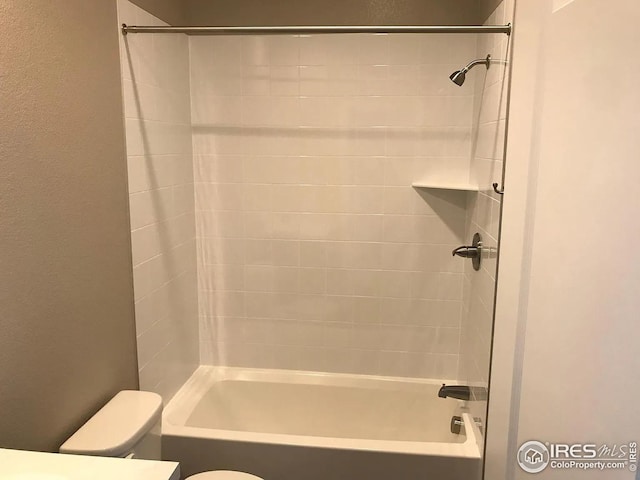 bathroom featuring washtub / shower combination, a textured wall, and toilet