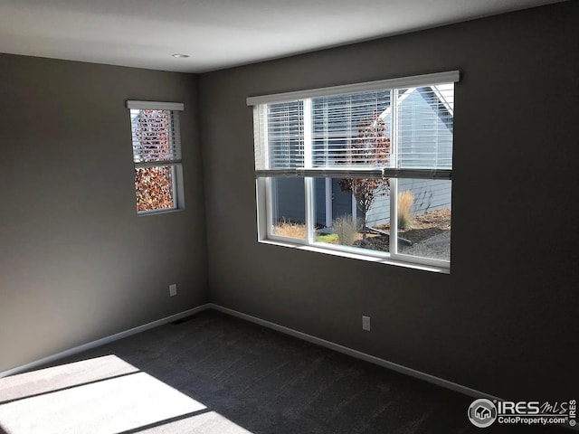spare room featuring dark colored carpet and baseboards
