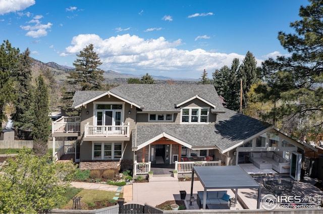 rear view of property featuring roof with shingles, a deck with mountain view, fence, and stone siding