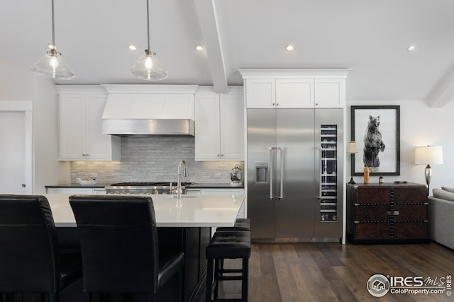 kitchen featuring white cabinets, beam ceiling, wall chimney exhaust hood, backsplash, and built in refrigerator